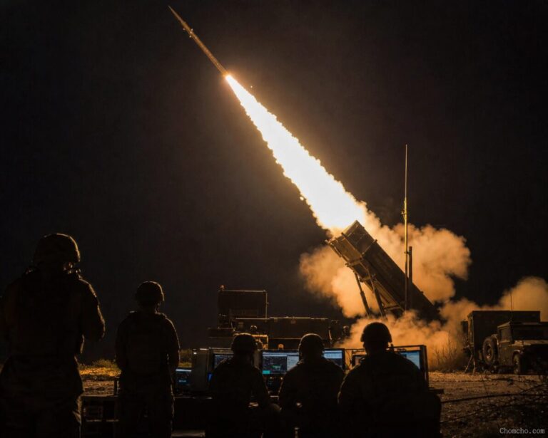 A Patriot interceptor missile launching from its mobile launcher in a burst of flame and smoke, the trail rising into a dusk sky.